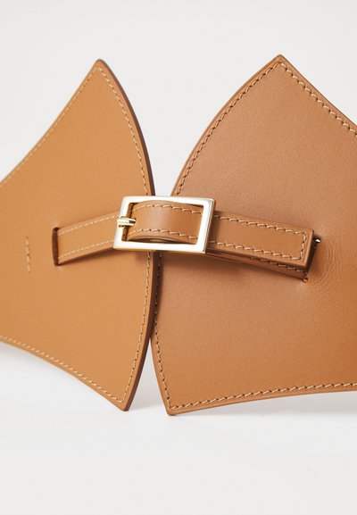 Cinturón de cuero marrón claro con extremos puntiagudos, que presenta una hebilla de metal dorado y detalles de costura. Textura suave y diseño minimalista.