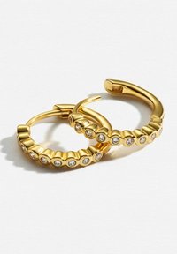 Guldtonade hoopsmycken med en texturerad design och cirkulära kristallaccenter längs framsidan. Slätt avslut, gångjärnsstängning.