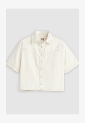 Chemisier court à manches courtes, écru, avec col pointu et coutures apparentes sur la poitrine et les manches.