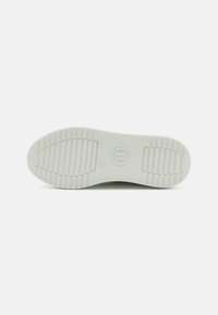 Hvit sneakersåle med et teksturert mønster, med horisontale striper for grep og et rundt logo i sentrum.