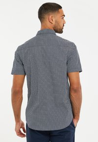 Kortærmet skjorte i marineblå med et geometrisk hvidt mønster. Har en button-down krave og en buet søm. Glat stofstruktur.