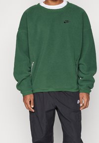 Zelená fleecová mikina s texturovaným povrchem, kulatým výstřihem a dlouhými rukávy. Má malé černé logo a boční zip.