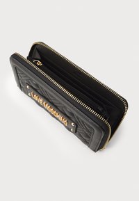 Carteira acolchoada preta com acabamentos em dourado, apresentando um proeminente logótipo "LOVE MOSCHINO". Fecho com zip e vários compartimentos interiores.