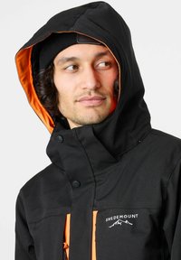 Zwarte weersbestendige jas met een oranje binnenvoering, voorzien van een ritssluiting aan de voorkant, twee voorkruippockets en logo-detail op de borst.
