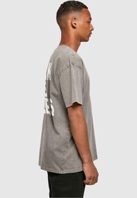 Grijze oversized t-shirt met een vervaagde afwerking, voorzien van witte tekst op de achterkant. Korte mouwen en een ontspannen pasvorm.