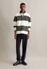 White and dark green striped sweatshirt with a zip neck, paired with black jeans and black boots. Smooth texture, relaxed fit.