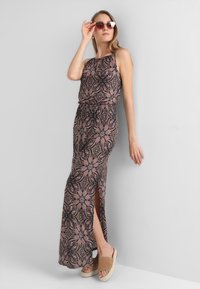 Vestido maxi con un estampado floral en rosa, negro y azul. Diseño sin mangas, cintura elástica, abertura lateral, combinado con sandalias beige y gafas de sol.