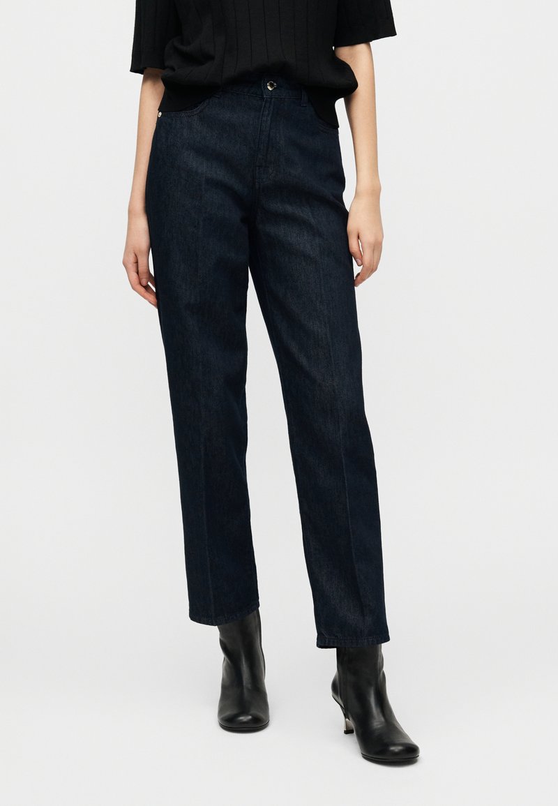 Σκούρο μπλε τζιν με ίσια γραμμή, με κουμπιά μπροστά και κλασικό σχέδιο με πέντε τσέπες.