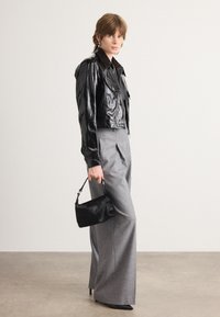 Fekete fényes cropped dzseki, szürke bővebb nadrág, kis fekete táska a kezében. Kiemelkedő fényes felület és testre szabott illeszkedés jellemzi.