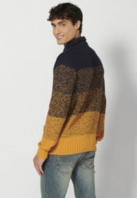 Suéter de punto con cuello alto, que presenta un diseño degradado en azul marino, mostaza y patrones texturizados. Puños y dobladillo acanalados.