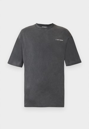 T-shirt gris charbon à manches courtes avec col rond et petit texte blanc "// NOT SORRY" sur le côté gauche de la poitrine.