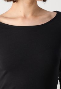 Top noir à manches longues avec un décolleté large en forme de rond. Fabriqué en tissu doux et extensible, il présente une texture lisse et un design simple.