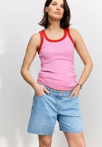 Pink ribbet tanktop med rød kant, kombineret med lyseblå denimshorts. Outfitet har en afslappet pasform og minimalistiske detaljer.