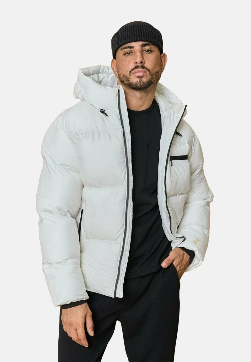 Doudoune en gris clair avec une capuche, fermeture éclair à l'avant et poches zippées. Présente un design matelassé et des accents noirs. Portée par-dessus une chemise noire.