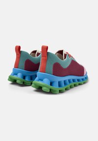 Colorful sneakers featuring a textured mesh upper in green, maroon, and blue with a chunky green sole and red accents on the heel.