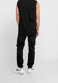 Černý bezrámový top, uvolněný střih, v kombinaci s tmavými džíny. Obuv zahrnuje bílé tenisky Nike se zelenými akcenty.