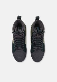 Wysokie sneakersy w ciemnozielonym i szarym wzorze materiałowym, z grubymi sznurowadłami, teksturowanymi gumowymi podeszwami i wyraźnymi czubkami.