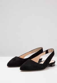 Bailarinas negras de ante con talón descubierto, punta afilada y tacón bajo. Presentan un diseño recortado en los laterales y un forro interior beige suave.