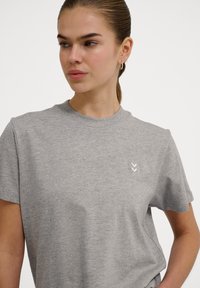 Grå bomulds t-shirt med korte ærmer, rund hals og et lille hvidt chevron-logo på venstre bryst. Blød tekstur og afslappet pasform.