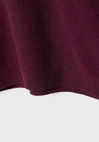 Tiefviolett gestrickter Stoff mit Rippensaumdetails, der Textur und Falten gegen einen schlichten, hellen Hintergrund zeigt.