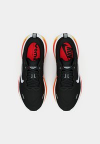 Μαύρα αθλητικά παπούτσια με υφή στο επάνω μέρος, λευκό λογότυπο Swoosh, κόκκινες και κίτρινες λεπτομέρειες στη σόλα και μαύρα κορδόνια. Άνετη σχεδίαση για εφαρμογή.
