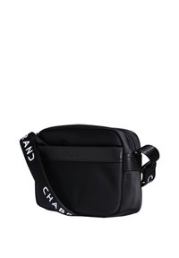 Sac à bandoulière en tissu noir avec fermeture éclair, doté d'une poche avant et d'une sangle réglable avec texte blanc. Texture lisse et forme rectangulaire.