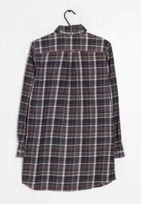 Košile s dlouhým rukávem s černobílým kostkovaným vzorem. Obsahuje límec, knoflíkové manžety a rovný spodní lem. Vyrobeno z tkané bavlněné látky.