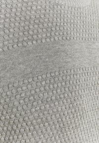 Šedá pletená látka s texturovaným vzorem obsahujícím malé vystouplé tečky. Vloženy hladké části, které ukazují rozmanitý povrch.