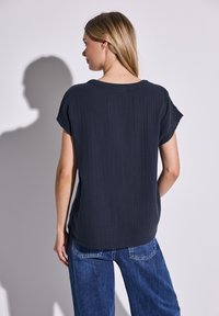 Dunkelgraues T-Shirt mit kurzen Ärmeln aus strukturiertem Stoff, lockerer Passform und rundem Halsausschnitt, kombiniert mit blauen weiten Jeans.
