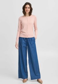 Cardigan rosa chiaro con colletto rotondo e bottoni frontali, abbinato a pantaloni in denim blu larghi e scarpe Beige. Design semplice e casual.