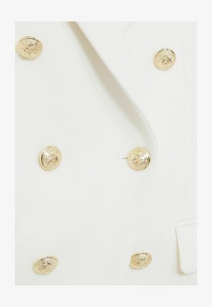 Dubbla bröstknappar vit kavaj gjord av välsydd tyg med guldfärgade präglade knappar och subtila fickdetaljer.