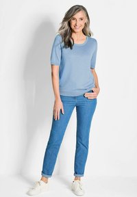 Himmelblaues, kurzärmliges Sweatshirt aus weichem Strickmaterial; kombiniert mit dunkelblauen, figurbetonten Jeans und weißen Sneakers. Einfaches, lässiges Outfit.