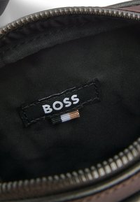 Svart tyginteriör i en väska med en "BOSS"-tagg med vit logotyp och färgade accenter, samt en texturerad dragkedjekant.