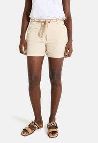 Shorts beiges avec des ourlets retournés, taille élastique avec cordon de serrage, associés à des sandales marron avec une sangle à motif léopard.