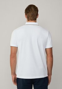 Polo bianco realizzato in cotone liscio con un bordo scuro a contrasto su maniche e colletto. Progettato con una vestibilità classica e maniche corte.