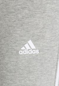 Grå sportbyxor i mjukt tyg med en vit Adidas-logotyp. Designen är enkel med en slät yta och inga ytterligare mönster.