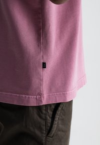 Roze katoenen T-shirt met korte mouwen en rechte zoom, voorzien van een klein zwart logotag en gecombineerd met donkere broeken.