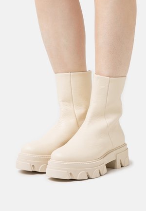 Krämfärgade läderankelstövlar med en slät yta, som har en tjock, kraftig sula med en vågig design och minimal sömnadsdetalj.