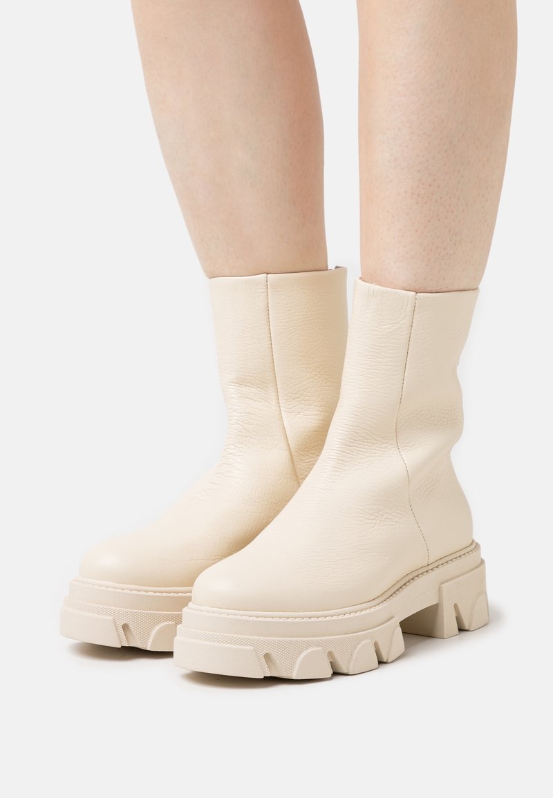 Cream leather ankle boots with a smooth texture, featuring a thick, chunky sole with a wavy design and minimal stitching detail.