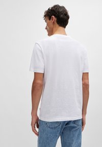 Valkoinen lyhythihainen t-paita, joka on valmistettu röpelöisestä puuvillasta, ja jossa on pyöreä pääntie ja rento istuvuus. Paita on yhdistetty vaaleansinisiin farkkuihin.