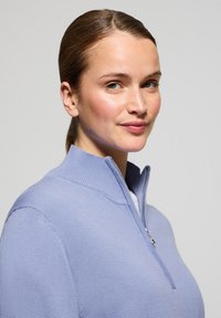 Ljuslila zip-tröja med ribbad krage. Mjuk stickad textur, figurnära design och synliga sömmar på ärmarna.