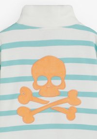 Tissu rayé blanc et bleu avec un motif de tête de mort et os croisés orange cousu sur la surface, centré sur l'objet.