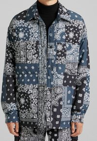 Långärmad skjorta med lappar av blå och svarta paisleymönster. Tillverkad av smidigt tyg med knäppning och två bröstfickor.