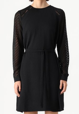 Sort kjole med tekstureret stof, lange gennemsigtige blonder ærmer med zigzag mønster og et matchende stofbælte ved taljen.