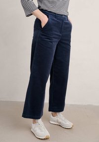 Marina kordflorsbyxor med vida ben, sidofickor, knappstängning och mjuk textur, kombinerat med vita sneakers.