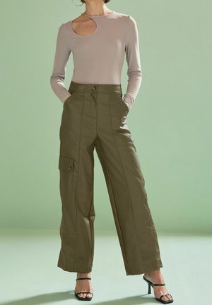 Top beige à manches longues avec un détail découpé et un pantalon cargo large vert olive comportant une poche latérale et des coutures visibles. Sandales noires à talons avec lanières.