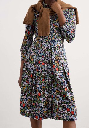 Robe midi à imprimé floral avec manches longues, fermeture boutonnée devant, et un pull marron posé sur les épaules.
