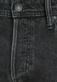 Tuvuma melnā džinsu tuvplāns ar redzamām pogām un jostas cilpas šuvēm.