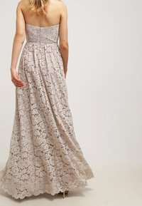 Long, strapless lace dress in light beige with floral patterns, flared silhouette, and a discreet zipper at the back. Smooth, textured finish.