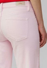 Jeans rosa chiaro con un design a cinque tasche, vestibilità slim e un piccolo etichetta con marchio sulla vita. Il tessuto ha una texture morbida.